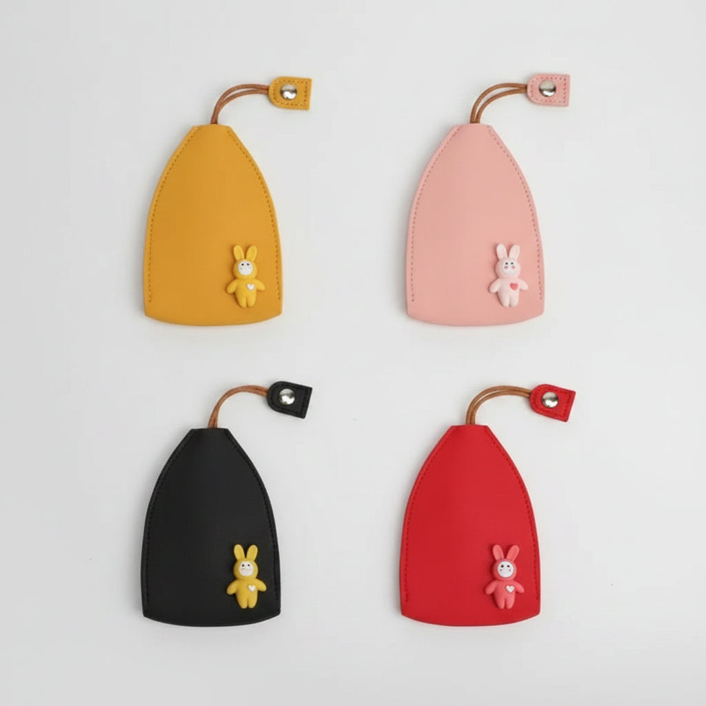 Four small leather keychain pouches arranged in a 2x2 grid on a white background, each with a curved strap and snap closure and a small bunny charm. The pouches are shown in yellow, pink, black, and red, with matching and contrasting bunny charms.