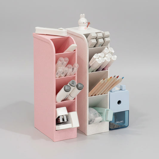 A pink and white multi-layer desk organizer shown on a tabletop with overlaid feature callouts and text, including 'Using height space Save desktop Space,' 'Three layers for the pencil,' and 'Small compartment for tools.' The organizer contains pens, pencils, sticky notes, and a small blue pencil sharpener.